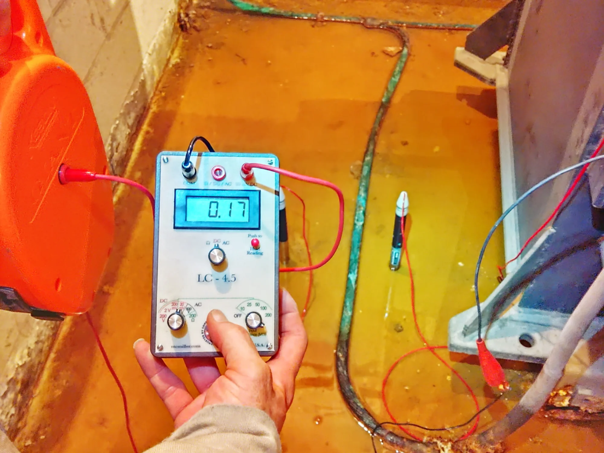 Hand holding a corrosion-potential meter taking a reading in a flooded distribution vault