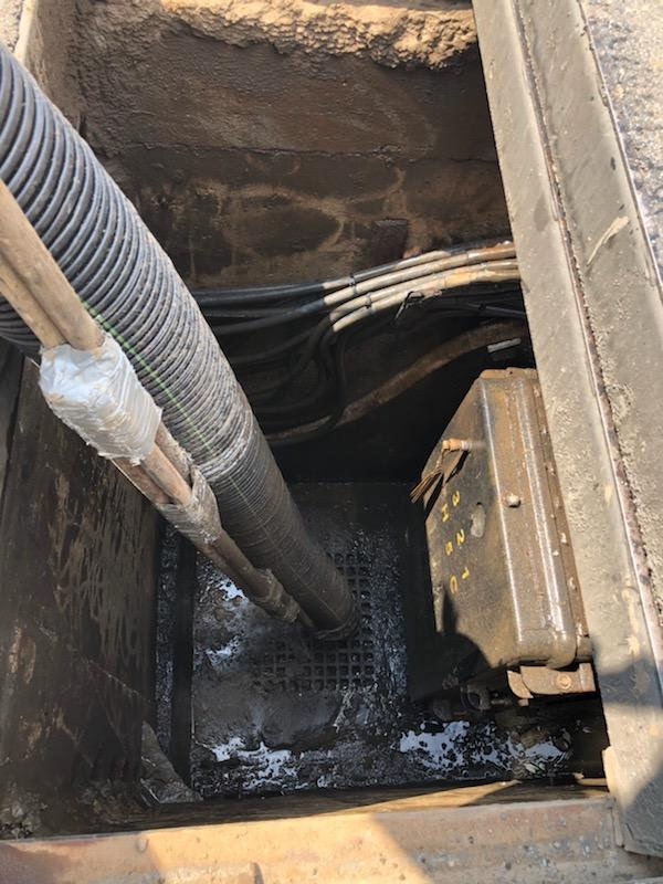 Corrugated cable conduits entering a network-transformer vault, with debris and water on the floor