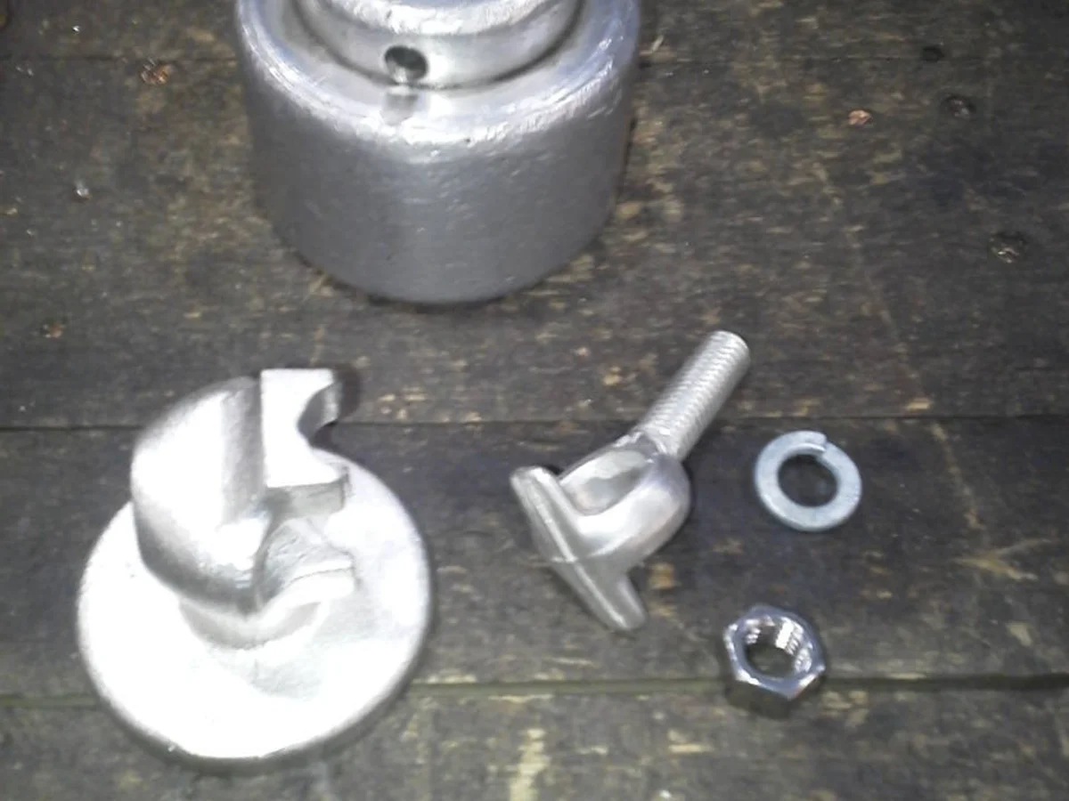 Galvanized cast-aluminum hardware with eye-bolt fastener, washer, and ground strap on a shop bench